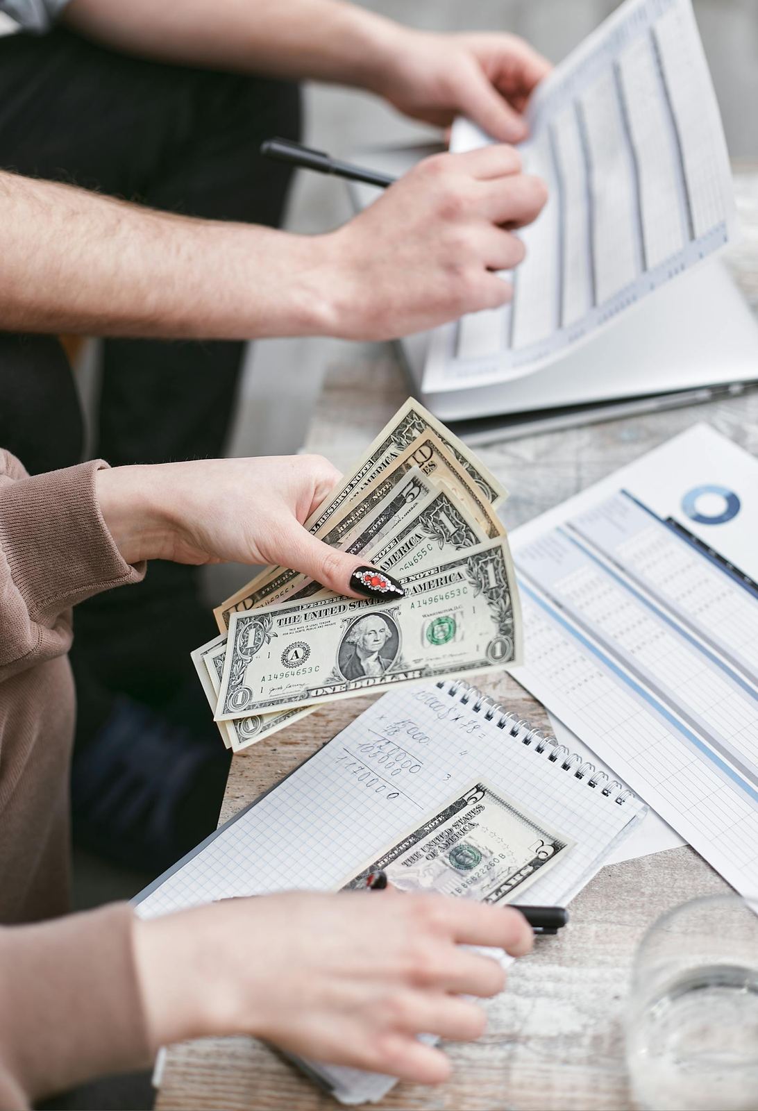 Two people counting cash and reviewing payroll paperwork at a desk